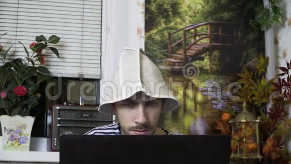 一个穿着背心和浴帽的男人坐在笔记本电脑前惊讶地睁大眼睛视频的预览图
