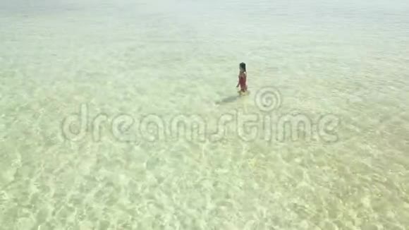 一名年轻女子在海滩上行走的空中追踪镜头无人机飞来飞去视频的预览图