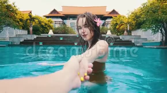 一个年轻的微笑的女人湿漉漉的头发牵着男朋友在游泳池里的手视频的预览图