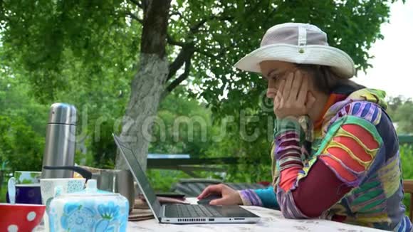 那个戴帽子的女孩在街上沉思地坐在笔记本电脑前视频的预览图