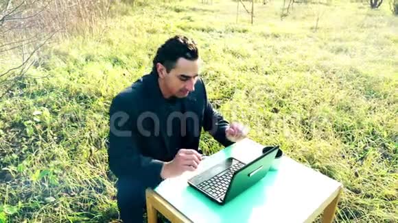 年轻有魅力的商人穿着笔记本电脑坐在外面绿色草地上办公室在户外自由职业视频的预览图