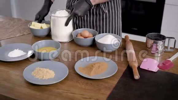 这个人是个穿围裙的厨师双手戴手套桌子上有纸杯蛋糕的配料会有面团视频的预览图