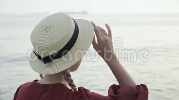 日落时分一个穿着夏红色连衣裙和草帽的白人女孩坐在海滨的近景中视频的预览图