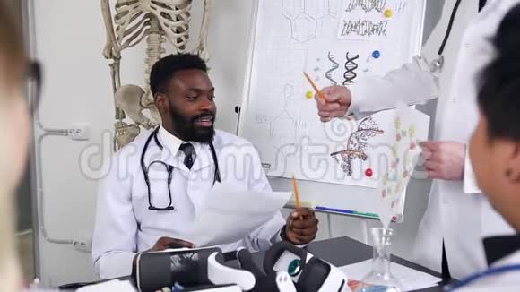 英俊的微笑着的非裔美国医生坐在医院的柜子里的桌子旁解释的感觉视频的预览图