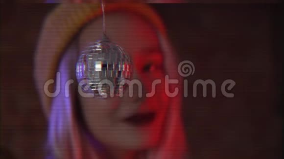 美丽的女人有着不寻常的时髦粉红色头发戴着黄色帽子手里拿着小迪斯科球圣诞树玩具霓虹灯视频的预览图