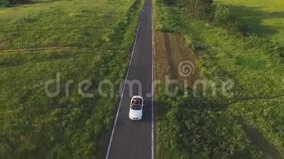 空中拍摄白色敞篷车骑过空的乡村道路四位年轻的无法辨认的女性视频的预览图