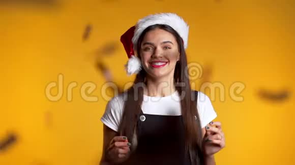 兴奋的女孩带着圣诞老人的帽子鼓掌为黄色的纸屑雨而高兴视频的预览图