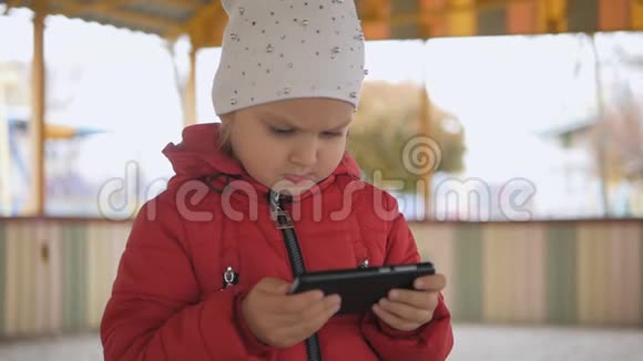 一个穿着红色夹克的小女孩专注地看着智能手机屏幕上的卡通视频的预览图