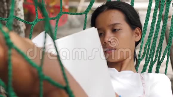 一个年轻漂亮的女人在吊床上休息和看书的肖像视频的预览图