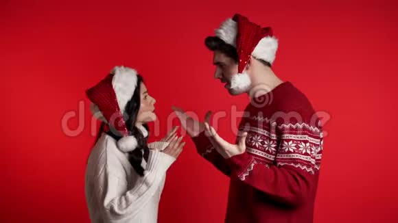 一对戴着圣诞帽的年轻夫妇在演播室的红色背景下激烈争吵视频的预览图