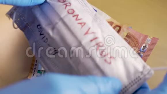双手戴着蓝色的医用手套在欧元钞票上戴上带有冠状病毒字样的口罩视频的预览图