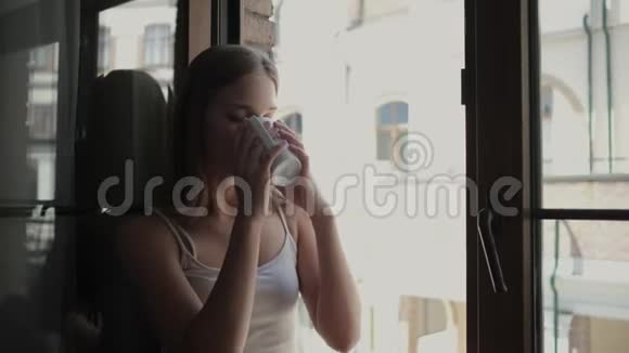 女人坐在敞开的窗台上喝茶视频的预览图