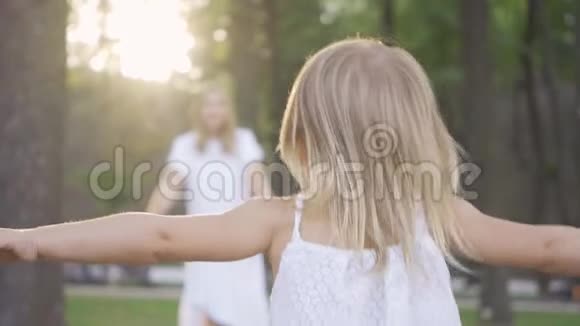 在阳光下小金发女孩朝她母亲跑去漂亮的年轻女子拥抱她的女儿视频的预览图