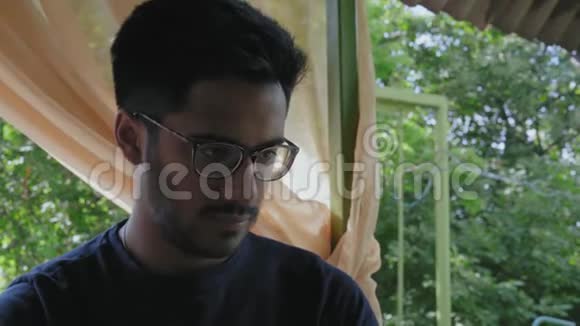 特写镜头戴眼镜的印度男人看着笔记本显示器坐在公园的桌子旁视频的预览图