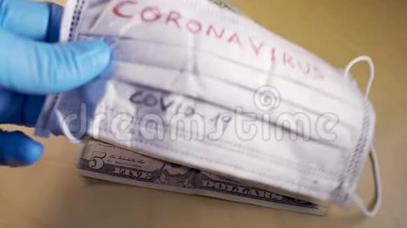 双手戴着蓝色的医用手套在钞票上戴上带有冠状病毒字样的口罩视频的预览图