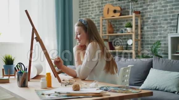一位年轻的女设计师在家中画画画架坐在公寓里视频的预览图