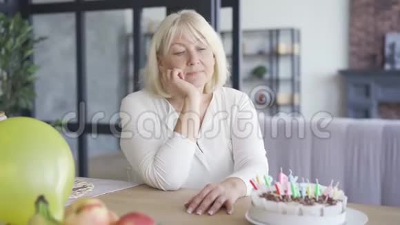 悲伤不快乐的成熟女人坐在桌子前的小生日蛋糕在埃姆比房间生日庆典视频的预览图