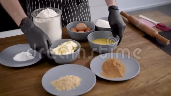 这个人是个穿围裙的厨师双手戴手套桌子上有纸杯蛋糕的配料会有面团视频的预览图