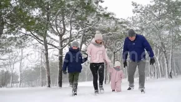 友好的全家人在降雪的情况下在冬天的森林里散步父亲母亲儿子和女儿视频的预览图