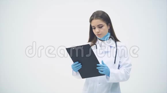 年轻的女实习生站在医用制服上拿着剪贴板看着镜头表情严肃视频的预览图