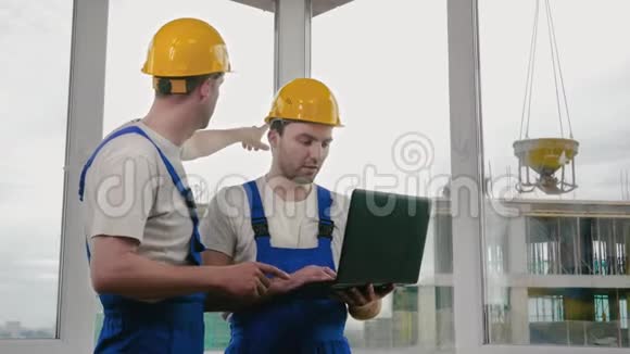 两名工人戴着防护头盔在笔记本电脑上工作视频的预览图