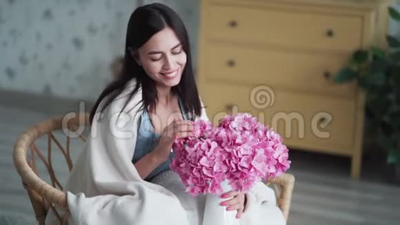 快乐的年轻女子坐在扶手椅上捧着一束鲜花嗅着它微笑着视频的预览图