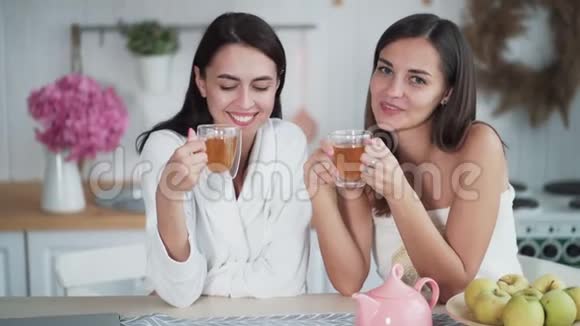 两个漂亮女孩早上在厨房喝茶看着镜头视频的预览图