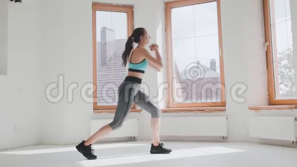 穿着运动服装跳跃的漂亮年轻健康的运动女孩在家做蹲视频的预览图