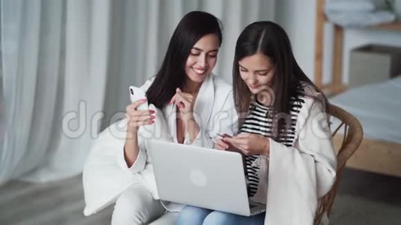 两个女人坐在卧室的椅子上手提电脑电话卡片和网上购物视频的预览图
