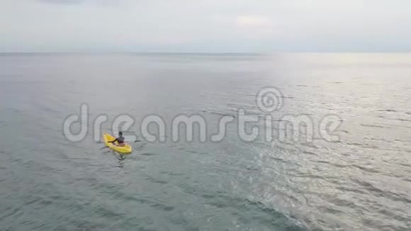 一个女人坐在皮划艇上坐在一艘船上的无人机镜头在海洋中冥想视频的预览图