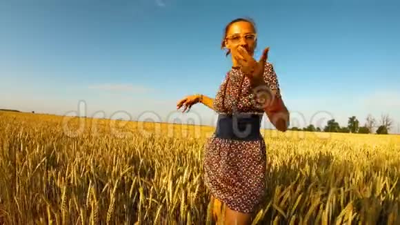 美丽的小女孩穿着短裙在风蓝天晴朗的日子里在黄色的麦田里翩翩起舞视频的预览图