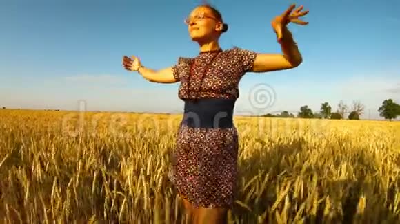 穿着短裙的女孩在风蓝天晴天的黄麦田间用手做美丽的传递视频的预览图