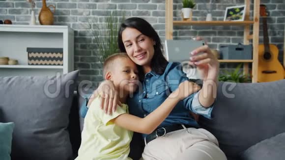 快乐的母子摆姿势拥抱智能手机微笑着自拍视频的预览图