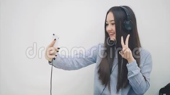有趣的年轻亚洲女孩站在耳机里听音乐自拍摆姿势做脸然后视频的预览图