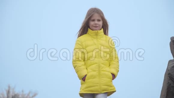 蓝天背景上一个穿着黄色外套的美丽高加索女孩的肖像可爱的小孩向外看视频的预览图