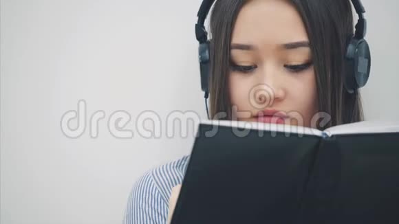 启发年轻的亚洲女孩坐在地板上戴着耳机听着音乐写作抬头看着相机视频的预览图