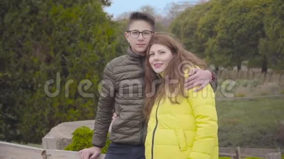 十几岁的白人男孩在秋天公园拥抱他可爱的母亲年轻的红发白种人女人和她的儿子摆姿势视频的预览图