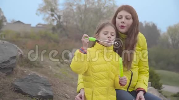 迷人的白人红发女人在秋天公园和小可爱的女孩玩肥皂泡快乐的母亲视频的预览图