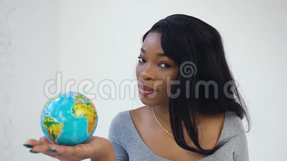 微笑着30岁深肤色的漂亮女人站在白色的背景上手里拿着小地球仪视频的预览图