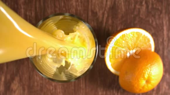 橙汁倒入一个玻璃站在木制的表面与新鲜的橙果片周围飞溅在慢M视频的预览图