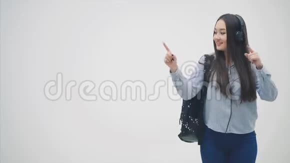 年轻的亚洲女孩戴着耳机背包挂在她的肩膀上手指指向交叉空间给予视频的预览图