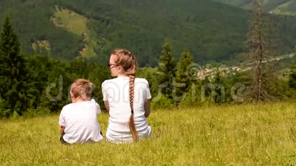 母亲和两个小儿子在绿林和群山的背景下在草地上玩耍视频的预览图