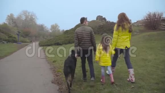 后景白种人母亲与她的小女儿穿着黄色外套和大儿子在秋天公园散步欧洲视频的预览图