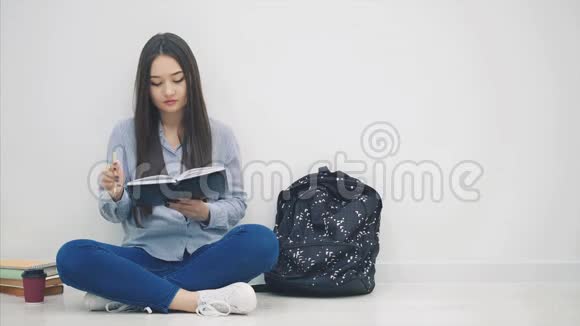 灵感来自年轻的亚洲女孩坐在地板上写完字从背包里拿出手机和耳机然后视频的预览图
