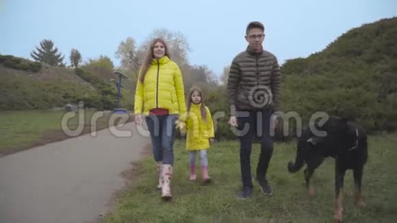 白人一家人带着他们的大黑狗在秋天公园散步怀孕的母亲和女儿一起散步视频的预览图