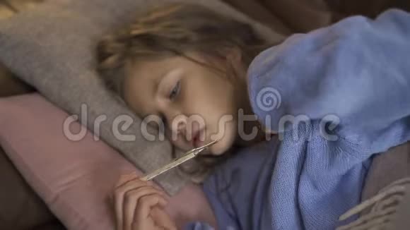 年轻的白种人女孩穿着蓝色毛衣带温度一个生病的黑发小孩躺在温暖的房间里视频的预览图