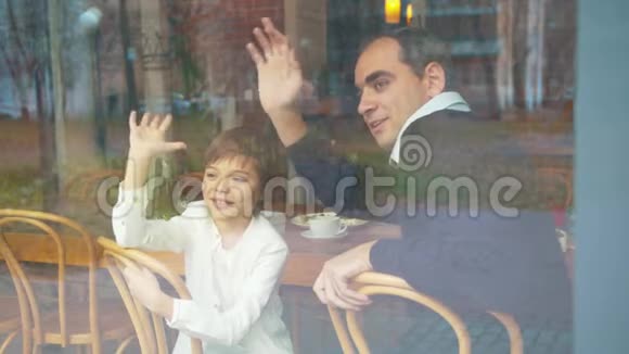 父亲和儿子在咖啡馆里透过窗户向某人挥手视频的预览图