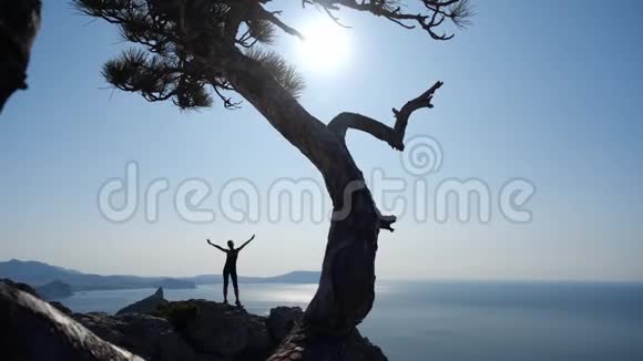 运动的女人站在悬崖上在晴朗的蓝天上欣赏大海的景色和耀眼的阳光视频的预览图