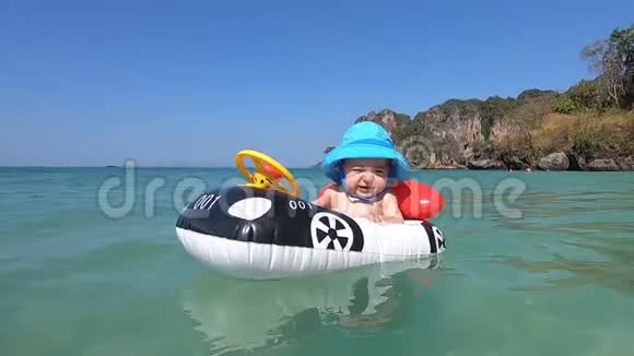 在开阔的大海和群山的背景下一个穿着蓝色巴拿马的快乐宝宝在一艘充气汽车形状的床垫船上游泳视频的预览图