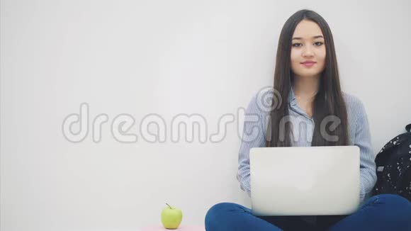 可爱的年轻亚洲女士坐在地板上手提电脑在洛托斯的位置手指指向一边视频的预览图